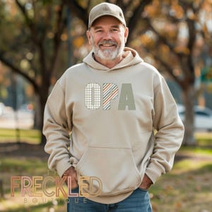May include: A beige hoodie with a patterned design that spells out "OPA" in large letters.