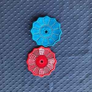 May include: Two embroidered fabric coasters, one blue and one red, with a circular design and a hole in the centre.