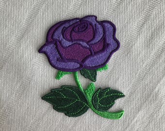 May include: Purple embroidered rose with green leaves and stem. The rose is a single bloom with a layered design. The leaves are detailed with a stitched outline.