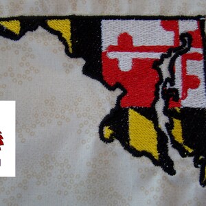 May include: Embroidered patch of the state of Maryland with the state flag design. The flag is yellow, black, and red with a white cross. The outline of the state is black. The patch is on a white fabric background.