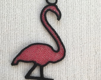 May include: A pink flamingo with black outlines, made of fabric with a mesh texture. The flamingo is standing on one leg with its head bent back.