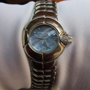 May include: A silver watch with a blue face and a silver band. The watch face has the words "paco rabanne" printed on it.