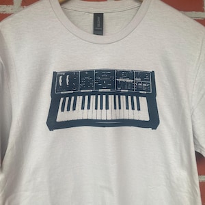May include: A white t-shirt with a black and white graphic of a vintage synthesizer keyboard.