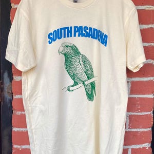 May include: A white t-shirt with a green parrot illustration and the text "SOUTH PASADENA" in blue.