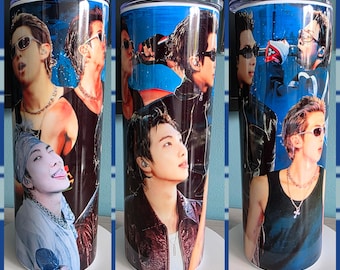 May include: A stainless steel tumbler featuring a collage of images of a male celebrity. The images are set against a blue background. The tumbler has a silver lid and is designed to keep beverages cold or hot.