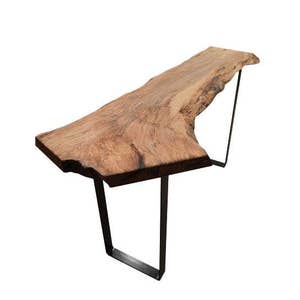 May include: A live edge wooden table with a natural, irregular edge. The tabletop is supported by a black metal frame. The wood has a warm, brown tone with visible grain patterns. The table is approximately 48 inches long.