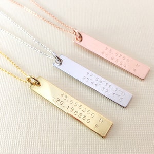 May include: Three gold, silver, and rose gold necklaces with bar pendants engraved with coordinates. The coordinates are 35.6766N 88.8588 W, 37°58′11.1 23°44′32.5"E, and 43.656260 N -70.198880 W.