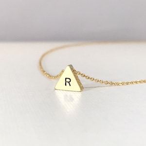 May include: A gold chain necklace with a small gold triangle pendant featuring the letter "R" engraved on it.
