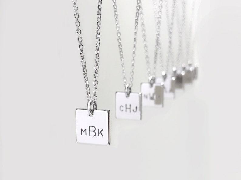 May include: A set of silver necklaces with square pendants, each engraved with different initials. The initials on the pendants are MBK, CHJ, and others.
