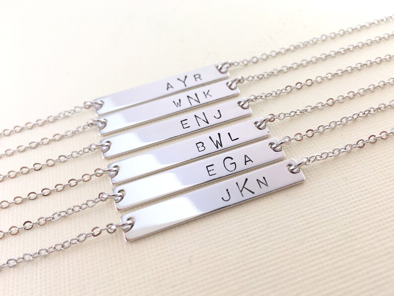 May include: Six silver bar necklaces with different names engraved on each bar: AYR, WNK, ENJ, BWL, EGA, JKN.