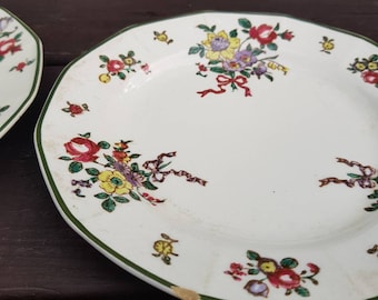 Puede incluir: Un plato de cerámica blanco con un borde verde y un patrón floral. Las flores son rojas, amarillas, rosas y moradas. El plato tiene un borde festoneado.