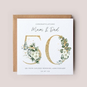 May include: A white card with gold glitter and green floral accents. The card says "Congratulations Mum & Dad 50 On your golden wedding anniversary 22.07.23"