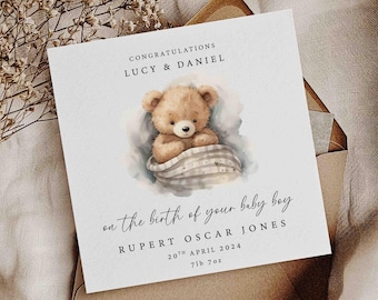 May include: A white card with a watercolor illustration of a brown teddy bear wearing a blue and white blanket. The card reads "Congratulations Lucy & Daniel on the birth of your baby boy Rupert Oscar Jones 20th April 2024 716 702".
