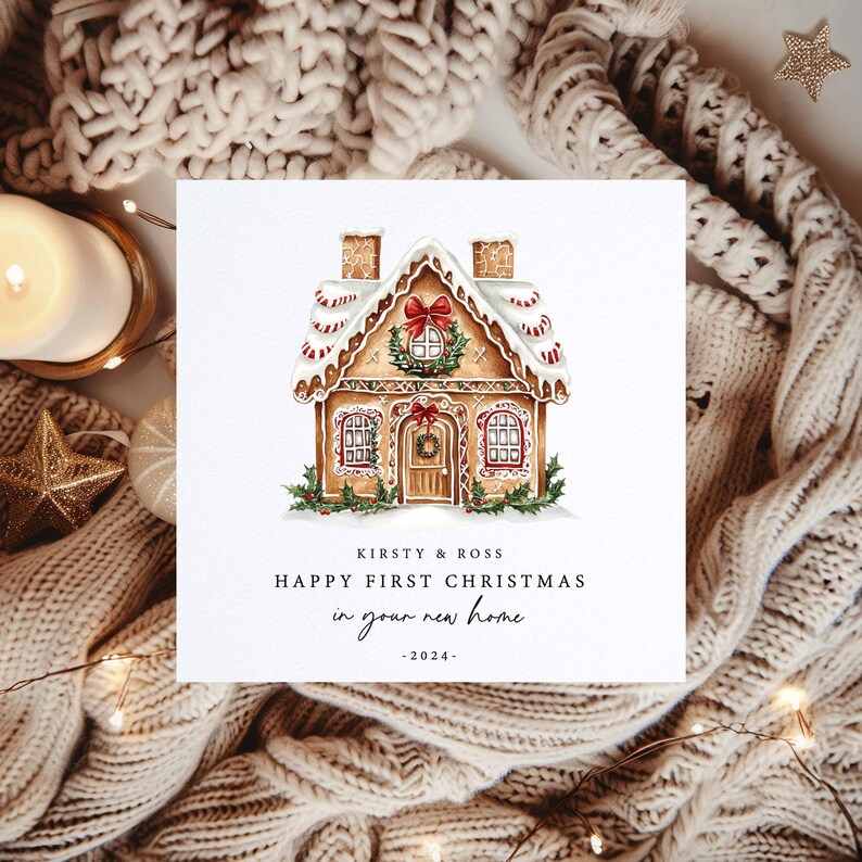 A square Christmas card with a gingerbread house picture on it. The text has the couple's names and says 'Happy First Christmas in your new home' with the year underneath.