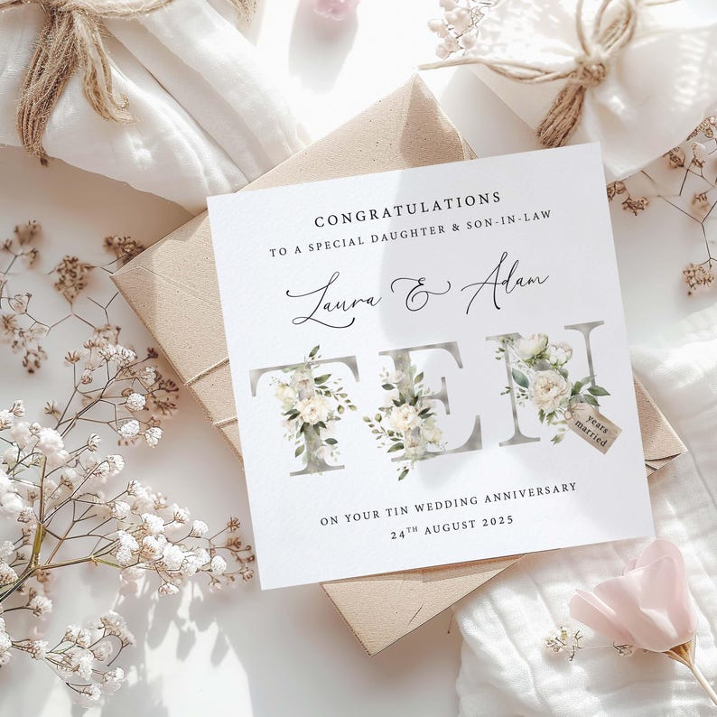 A personalised anniversary card for a 10th Wedding Anniversary. Has the couples names and date on it and the words 'Ten' written in words with white flowers and botanical leaves around the words.