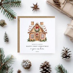 May include: A Christmas card with a gingerbread house illustration. The card reads "Kirsty & Ross, Happy First Christmas in your new home - 2024." The card is surrounded by pine needles, pine cones, and wrapped gifts.