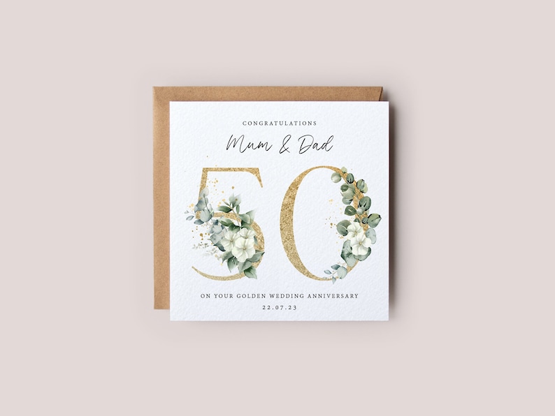 May include: A white card with gold glitter and green floral accents. The card says "Congratulations Mum & Dad 50 On your golden wedding anniversary 22.07.23"