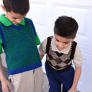 May include: Two children wearing knitted vests. One vest is green and blue striped, over a green collared shirt and khaki pants. The other vest is brown and white, over a tan collared shirt and blue pants. The children are standing in front of a white door.