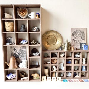 May include: A display of vintage collectibles in wooden compartments. Items include a brass plate, a teapot, a white cat figurine, and other small objects. The word "LOVE" is spelled out using letter tiles.
