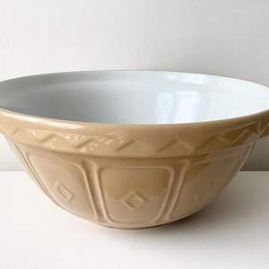May include: A large, tan ceramic mixing bowl with a white interior. The bowl features a decorative rim and vertical grooves. This traditional bowl is designed for mixing ingredients in the kitchen.