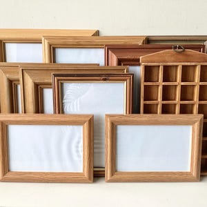 May include: A selection of wooden picture frames in various sizes and shades of brown. Some frames are rectangular, while others have a square grid of small compartments. The frames have white interiors.