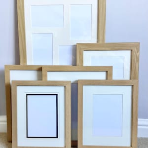 May include: A selection of wooden picture frames with white mounts. The frames are in various sizes and shapes, including multi-aperture designs. The wood has a light, natural finish. Some frames have a black border.
