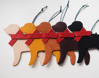 May include: Five dog-shaped ornaments in a row, each with a red scarf and green string for hanging. The dogs are in shades of beige, yellow, orange, brown, and black. These ornaments are likely for a Christmas tree or other holiday decor.