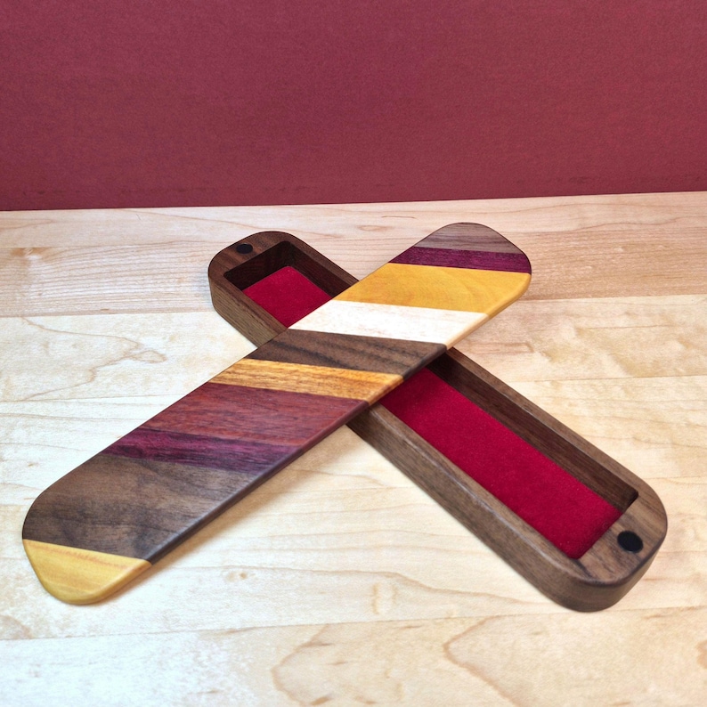 May include: A rectangular wooden box with a sliding lid, featuring a multi-colored striped pattern of dark brown, purple, yellow, and white wood. The interior of the box is lined with a vibrant red velvet fabric, and the lid is partially open.