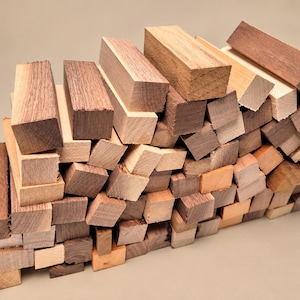 May include: A collection of rectangular wooden blocks in various shades of brown, tan, and cream. The pieces are stacked together, showcasing different wood grain patterns and textures across their smooth, cut surfaces.