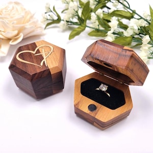 May include: Two wooden ring boxes. One box is closed and features a heart and cross design. The other box is open and shows a ring with a clear stone inside.