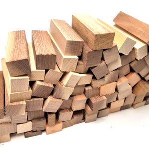 May include: A pile of various sized, unfinished wooden blocks in shades of brown and tan. The blocks are rectangular and square, with visible wood grain. The blocks are scattered, creating a textured surface.