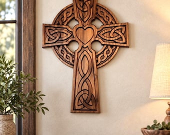 May include: A wall-mounted wooden Celtic cross featuring intricate knotwork patterns and a central heart cutout. The cross is crafted from dark brown wood with a smooth finish, showcasing detailed carvings throughout the arms and the circular ring.
