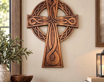 May include: A wall-mounted wooden cross featuring an intricate, carved Celtic knotwork pattern. The design consists of a central cross shape overlaid on a circular frame, with deep brown wood grain textures and smooth, rounded edges throughout.