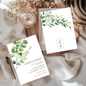 以下が含まれることがあります： 緑の植物イラストが施された白い結婚式の招待状。1枚のカードには「LAUREN & ANDREW」の名前と結婚式の詳細が記載されています。もう1枚のカードには緑の葉のデザインとイニシャル「L A」が描かれています。