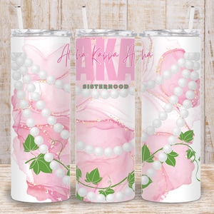 May include: Three pink and white stainless steel tumblers with a pearl and ivy design. The tumblers have the text "Alpha Kappa Alpha Sisterhood" printed on them.