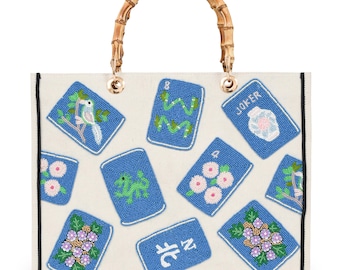 May include: Off-white tote bag with a bamboo handle and gold-tone hardware. The bag features blue beaded playing card designs with floral, bird, and snake motifs. A black border frames the bag's design.