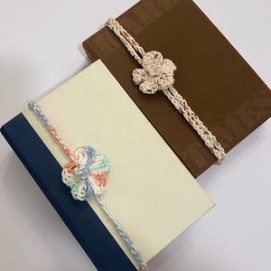 May include: Two books with crochet flower bookmarks. One is brown with embossed text, the other cream with a navy spine. The bookmarks have a flower design in cream, pink, and blue.