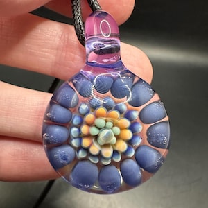 May include: A glass pendant necklace with a purple and blue flower design. The flower is made of small, round glass beads in shades of blue, green, orange, and white.