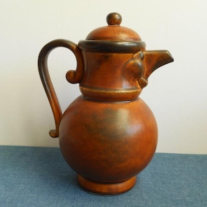 May include: A brown ceramic teapot with a lid and a handle. The teapot has a dark brown glaze and a light brown glaze. The teapot has a unique design with a bird-like spout.