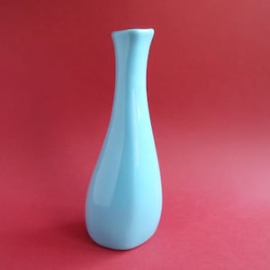 Könnte beinhalten: Eine hellblaue Keramikvase mit einem schlichten, eleganten Design. Die Vase hat einen schmalen Hals und einen breiten, abgerundeten Boden.