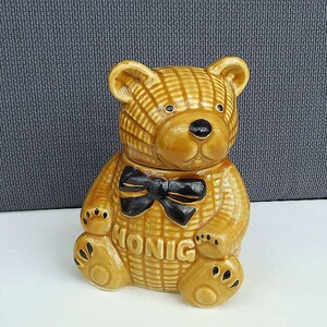 May include: A ceramic honey bear jar with a black bow tie. The jar is brown and has the word "Honig" written on it.