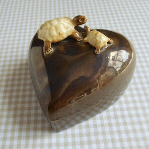 May include: A heart-shaped ceramic box with a brown glaze. Two small ceramic turtles are perched on top of the box.