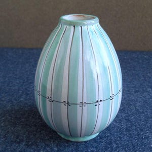 Peut inclure: Un vase en céramique avec un corps arrondi et un col étroit. Le vase est peint avec des rayures verticales en bleu clair, blanc et marron foncé. Le motif comprend une série de petits tirets foncés au milieu.
