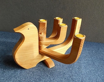 May include: A wooden candle holder shaped like a bird with five candle slots. The candle holder is made of light brown wood and has a natural finish.