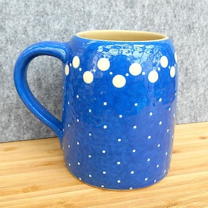 May include: A blue ceramic mug with white polka dots and a white border around the top. The mug has a handle.