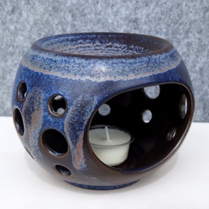 Op de afbeelding: Een ronde blauwe en bruine keramische oliebrander met een gat aan de zijkant voor een theelichtje. De brander heeft een getextureerd oppervlak en is versierd met kleine gaatjes.