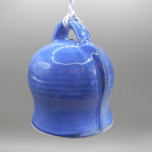 May include: A blue ceramic bell with a white string hanging from the top. The bell has a smooth, glazed finish and a slightly rounded shape.