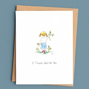 May include: A white greeting card with a watercolor illustration of a child with blonde pigtails wearing a white shirt, blue skirt, and red shoes, holding yellow flowers. The text "I Thank God For You" is printed in black ink below the illustration.