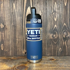 May include: A navy blue YETI Rambler 26 oz bottle with a black cap. The bottle has the YETI logo and text that reads "26 oz Bottle". The cap has a twist-to-open design.