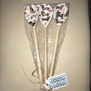 May include: Three wooden spoons with a white background and a dog pattern. The spoons are wrapped in clear plastic with white polka dots. A tag is attached to the spoons that reads "Handcrafted by TheCraftySpoonLady".
